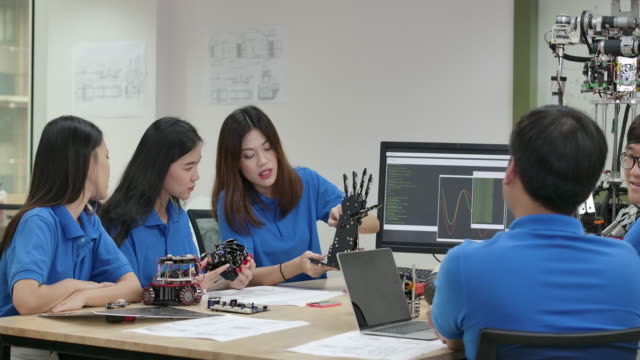 Equipo-de-ingenieros-electrónicos-jóvenes-que-colaboran-en-la-construcción-de-robots-en-el-taller.-Ingeniero-de-equipo-se-inicia-juntos-para-el-proyecto-de-robot.-Personas-con-concepto-de-tecnología-o-innovación.