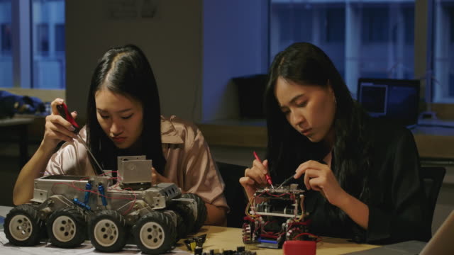Equipo-de-jóvenes-ingenieros-de-desarrollo-electrónico-construyendo,-probando,-arreglando-prototipos-de-robótica-por-la-noche-en-laboratorio.-Personas-con-concepto-de-tecnología-o-innovación.