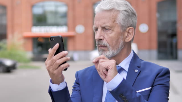 Outdoor-Portrait-of-Old-Businessman-Using-Smartphone