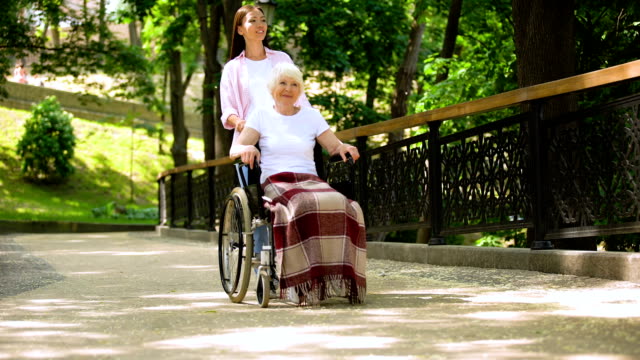 Nieta-empujando-a-la-anciana-en-el-jardín-del-hospital-en-silla-de-ruedas,-apoyo-y-cuidado