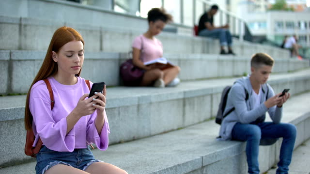 Estudiantes-universitarios-chateando-por-teléfonos-inteligentes,-adolescentes-que-se-desplazan-aplicación-de-la-red-social