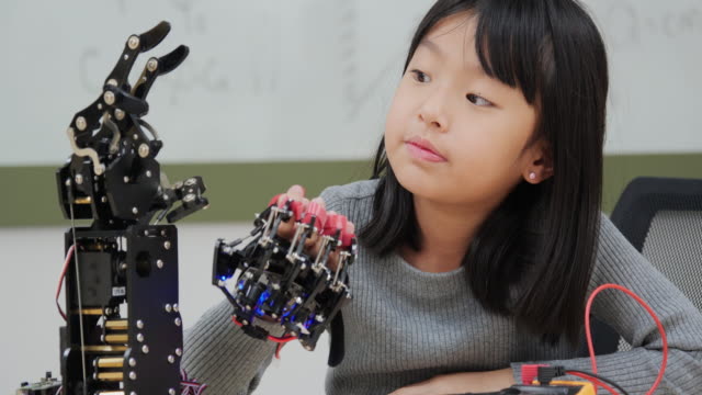 Little-Girl-está-jugando-con-el-brazo-robótico-en-una-escuela.-Ella-lo-está-controlando-con-su-mano.