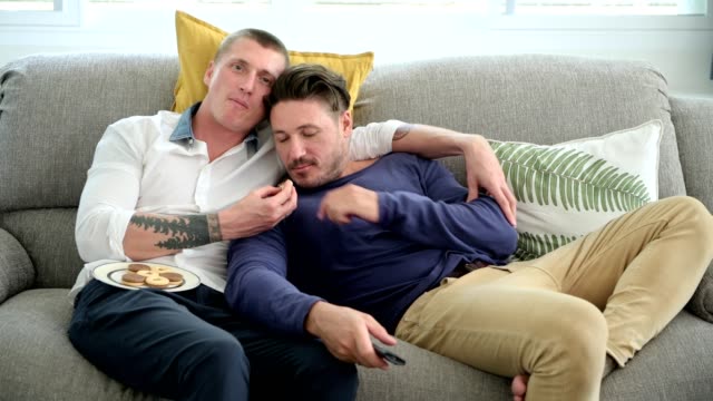 Gay-couple-relaxing-on-couch-watching-tv.-Enjoy-eating-food.