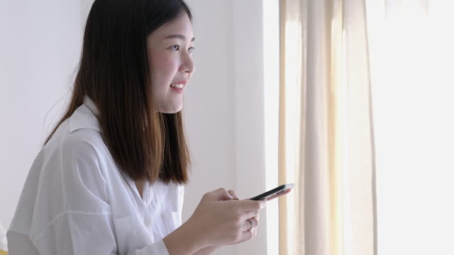 Mujer-asiática-escribiendo-aplicación-de-medios-sociales-en-el-teléfono-inteligente-en-la-habitación-de-la-cama.-Concepto-de-tecnología,-comunicación-y-compras.