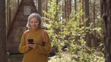 Hiker-Using-Mobile-Phone-near-Wooden-Cabin
