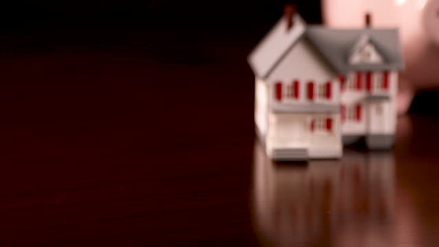 Pan-of-Piggy-Bank-and-Miniature-House-on-Dark-Wood-Surface