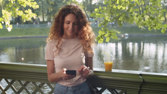 Mujer-feliz-usando-el-teléfono-en-el-parque-en-el-día-soleado