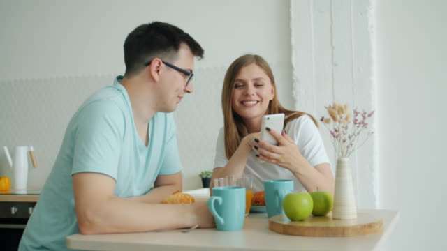 Slow-motion-of-man-and-woman-using-smartphone-at-kitchen-table-at-breakfast