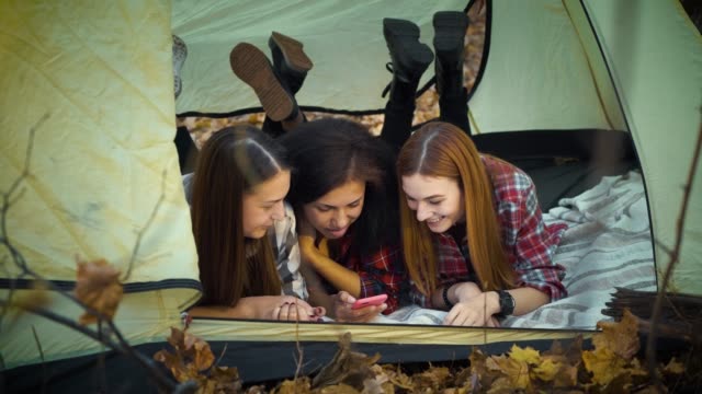 Glückliche-Touristen-mit-Smartphone-im-Zelt-liegen