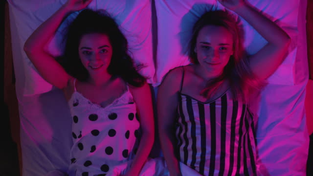 Attractive-girls-falling-on-bed-together-and-looking-at-camera,-night-seduction