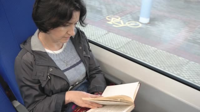 Mujer-caucásica-de-mediana-edad-montando-en-un-tren-leyendo-un-libro