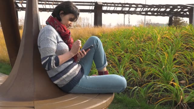 Caucasian-woman-sits-on-a-round-park-bench-with-a-phone-in-her-hands-clicks