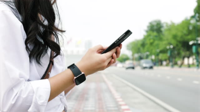 Close-up-hands-young-woman-typing-a-message-on-a-smartphone-while-standing-beside-the-street-in-urban.