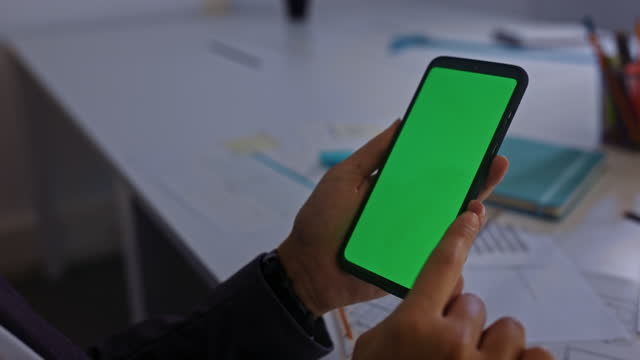 Business-woman-swiping-through-mobilephone-green-screen-at-her-office