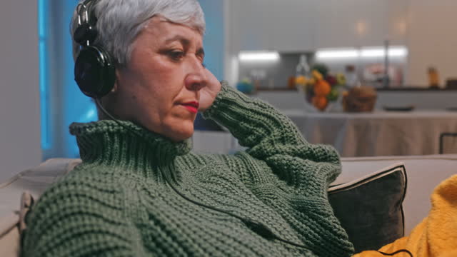 Mujer-mayor-con-auriculares-escuchando-música-sentada-en-el-sofá