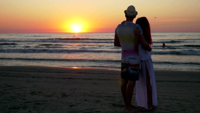 Paar-zu-umarmen-und-küssen-am-Ufer-von-einem-sandigen-Strand-bei-Sonnenuntergang