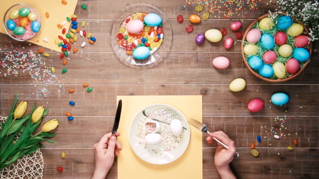 Man-holding-knife-and-fork-before-plate-with-easter-eggs-on-table-decorated-with-easter-eggs.-Top-view