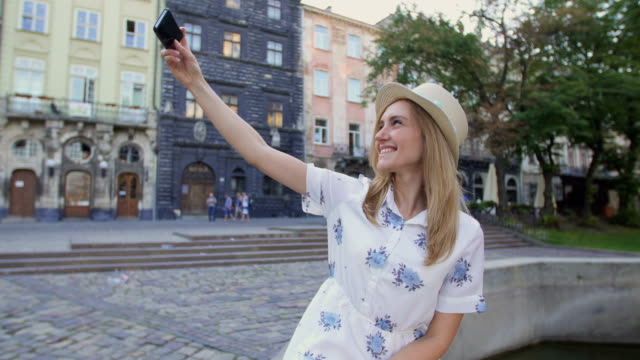 Junge-Mädchen,-die-Selfie-mit-Smartphone-sitzen-am-Brunnen-in-der-Stadt.-Glückliche-junge-Frau-lächelnd-posiert-für-Selbstporträt-mit-iPhone-Smartphone-Kamera.-Tourismus,-Instagram,-moderner-Technik.