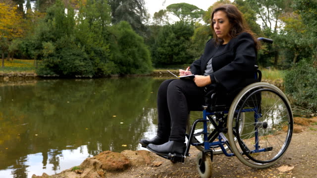 Retrato-de-mujer-en-sillas-de-ruedas-escribe-una-carta-de-amor-junto-al-lago