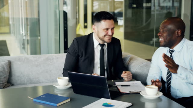 Two-businessmen-talking-ang-laughing-in-modern-cafe.-Business-colleagues-having-fun-and-joking-looking-at-laptop-computer-during-coffee-break
