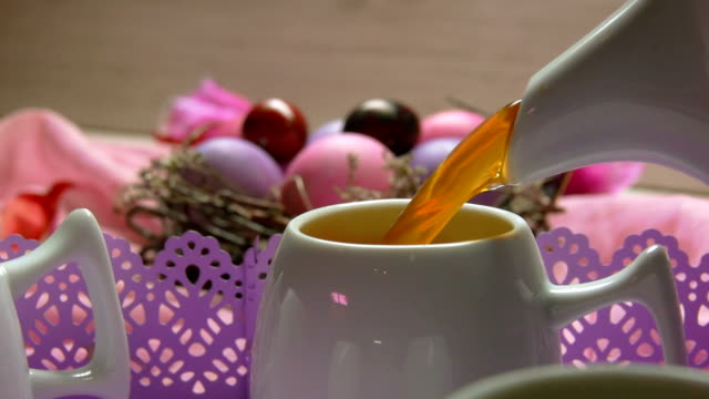 a-tea-poured-in-the-cup-on-the-background-of-colored-pink-Easter-egg-lies
