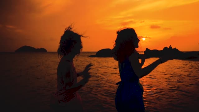 zwei-glückliche-Mädchen-tanzen-am-Strand-bei-Sonnenuntergang-in-Zeitlupe