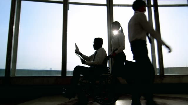Businesswoman-Pushing-Businessman-on-Wheelchair-in-Office-Building