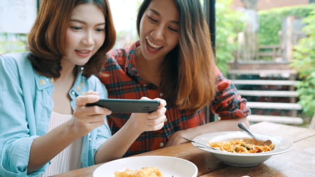 Happy-beautiful-Asian-friends-women-blogger-using-smartphone-photo-and-making-food-vlog-video-for-her-subscribers-and-her-channel-at-cafe.