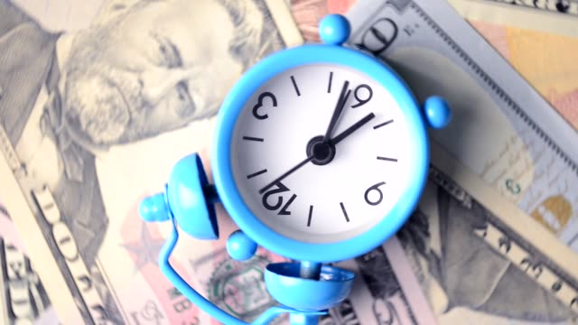 VIDEO,-Classic-alarm-clock-rotating-on-a-pile-of-cash-banknotes
