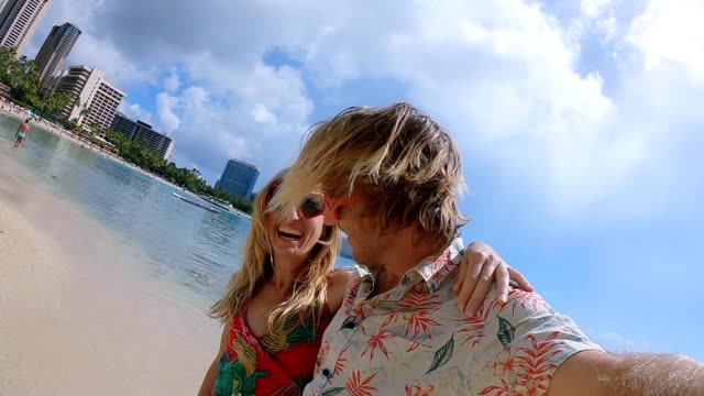 Par-tomar-autorretratos-en-la-playa-de-Waikiki-en-Honolulu,-Hawaii.-Selfie-granangular-punto-de-vista-de-la-playa-de-Waikiki.-Pareja-joven-tomar-autorretratos-con-el-corazón-en-forma-de-gafas-de-sol.-Cámara-lenta