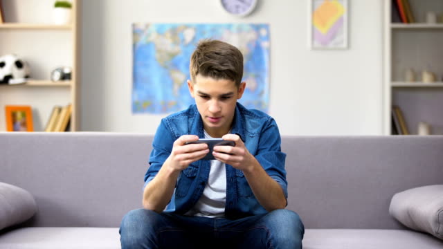 Gadget-addicted-Caucasian-teenager-playing-game-on-smartphone,-wasting-time