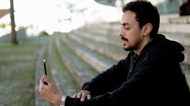 Seitenansicht-des-jungen-arabischen-Mannes,-der-im-Freien-ein-Video-Chat-hat