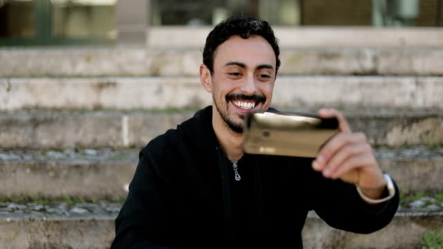 Front-view-of-Arabic-man-having-video-chat-outside,-waving-hand
