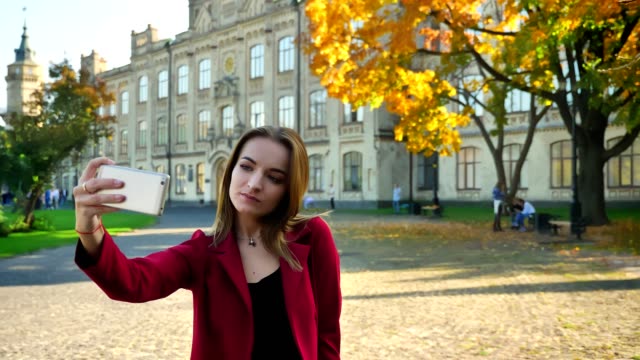 Junge-attraktive-Hündin-studend-macht-ein-Selfie-in-verschiedenen-Posen-vor-der-Universität-an-einem-sonnigen-Tag