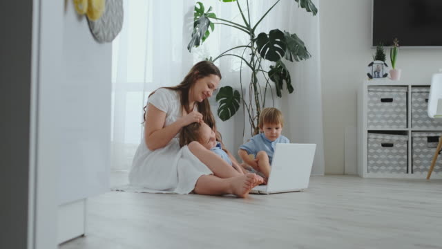 Moderno-apartamento-mamá-y-dos-hijos-sentados-en-el-piso-en-la-sala-de-estar-vistazo-a-la-pantalla-del-ordenador-portátil