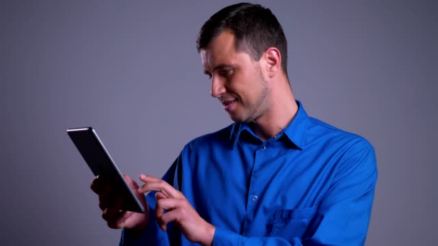 Closeup-portrait-of-adult-positive-caucasian-man-browsing-on-the-tablet-and-smiling-in-front-of-the-camera