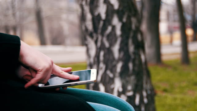 Junge-Frau-mit-Smartphone-auf-einer-Bank-im-Stadtpark