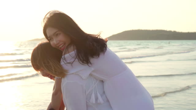 Young-Asian-LGBT-friends-playing-on-beach,-beautiful-women-friends-feel-happy-and-fun-relax-playing-on-beach-near-sea-sunset-in-evening.-Lifestyle-lesbian-friendship-travel-on-beach.-Slow-motion-shot.