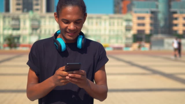fröhlicher-junger-Mann-mit-App-auf-Smartphone-zu-Fuß-auf-der-Straße