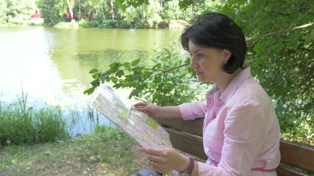 Morena-mira-un-mapa-de-papel-en-el-parque-cerca-del-estanque