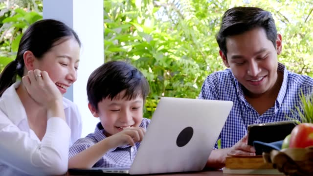 Familia-asiática-riendo-y-mirando-en-el-ordenador-portátil-digital-mientras-está-en-casa-Feliz-día-santo-tiempo