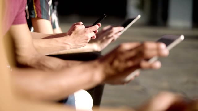 People-sitting-on-wooden-bench-and-using-digital-devices