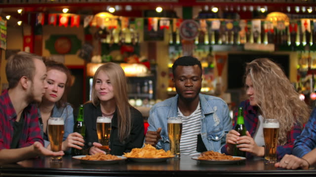 Multiethnische-Grappa-Freunde-sitzen-in-einer-Bar-und-trinken-Bier-und-haben-Spaß-beim-Plaudern-beim-Essen-von-Chips