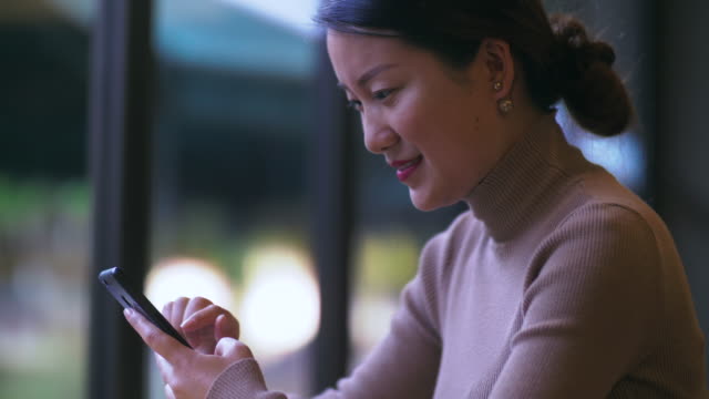 Fröhliche-junge-chinesische-Geschäftsfrau-mit-Handy-drinnen