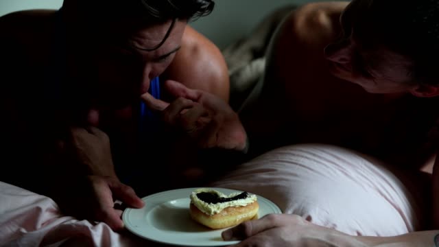 Gay-couple-enjoy-their-birthday-cake-together-in-bed.-Feeding-cake.