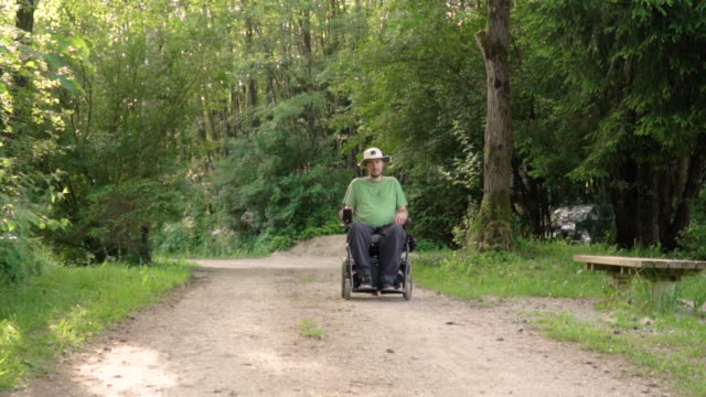 Slowmotion-portrait-of-disabled-young-man-in-a-wheelchair-observing-nature-around-him,-stopping-infront-of-the-camera