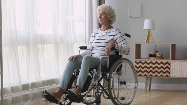 Thoughtful-sad-old-woman-sit-on-wheelchair-alone-at-home