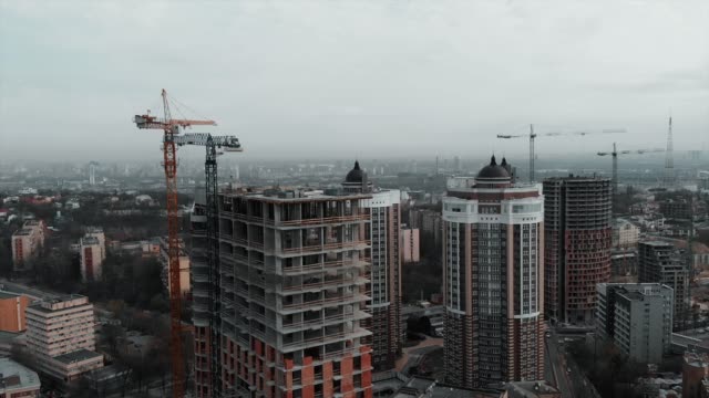 Group-of-caucasian-workers-in-orange-helmets-working-on-roof-of-unfinished-building.-Workers-at-construction-of-high-rise-residential-complex