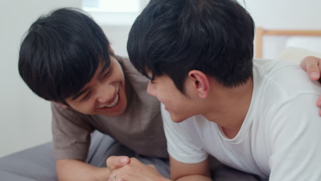 Schöne-asiatische-homosexuell-Paar-im-Bett-zu-Hause-sprechen.-Junge-asiatische-LGBTQ-+-Kerl-glücklich-entspannen-zusammen-verbringen-romantische-Zeit-nach-dem-Aufwachen-im-Schlafzimmer-im-modernen-Haus-im-Morgen-Konzept.