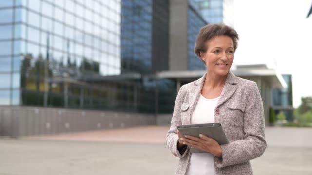 Glückliche-reife-Geschäftsfrau-denken,-während-digitale-Tablet-im-Freien